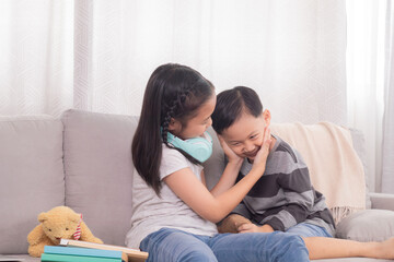 Two Asian siblings boy and girls having fun playing together on holiday at home while sister watches video games on modern technology laptop or doing homework on sofa, family relationship childhood