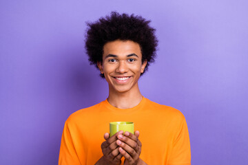 Photo of attractive positive man beaming smile arms hold morning coffee cup isolated on violet color background
