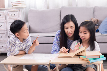 Cheerful Asian mother or teacher spend time with two siblings kids home school learning and practicing together in living room at home, free time children bonding relationship with mom parenthood