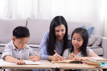 Cheerful Asian mother spend time with two sibling kids teaching homework drawing picture together in living room at home, free time children on holiday bonding happy relationship with mom parenthood