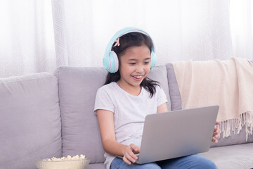 Asian sibling little girl playing game alone at home sitting on sofa using modern technology wireless laptop computer addiction, children studying homeschool learning typing keyboard listen to music