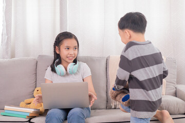 Asian sibling children play together bonding relationships on holiday at home, naughty boy kids are interested technology laptop want to watch video games while girl digital remote homeschool learning