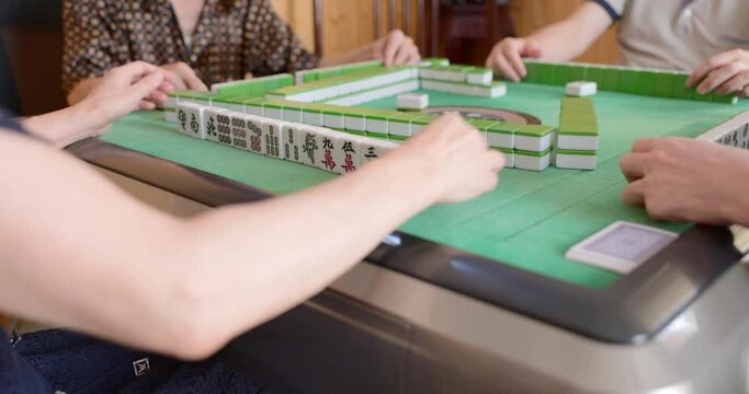 Selective focus with closeup of mahjong tiles and the player's hand tapping on gambling table.
