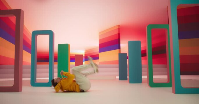 Dynamic Male Dancer in Bright Sweater Performing Swift Breakdancing Moves in a Colorfully Decorated Studio. Professional B-Boy Showcasing his Talent and Skills, Surrounded by Geometric Decoration