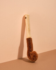 Wooden eco friendly brush curved shape for washing dirty dishes on a beige background.