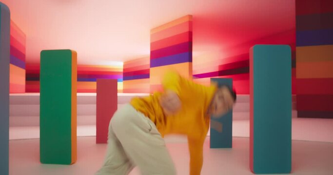 Dynamic Male Dancer in Bright Sweater Performing Swift Breakdancing Moves in a Colorfully Decorated Studio. Professional B-Boy Showcasing his Talent and Skills, Surrounded by Geometric Decoration