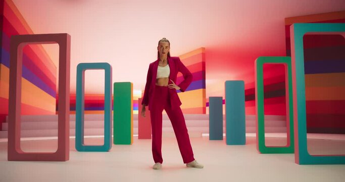Tracking Low Angle Portrait of a Fashionable Young Woman Performing a Catwalk in a Colorful Neon Studio. Stylish Female Walking Confidently In and Out of a Bright Lit Room