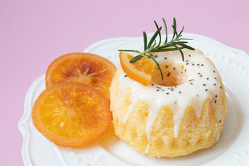 Orange bundt cake topped tangerines and rosemary on a white plate