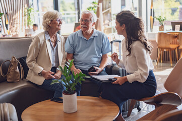 A hotel or travel agency representative is talking with a senior tourist couple offering various...