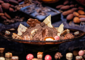 Broken chocolates of different colors in a beautiful glass vase. Unusual background.
