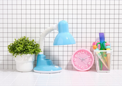 School and workplace. Blue lamp, pink clock and stationery. A green plant in a white pot.
