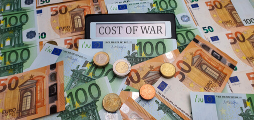 The cost of war. A calculator surrounded by euro bills and coins. The concept of militarization,...