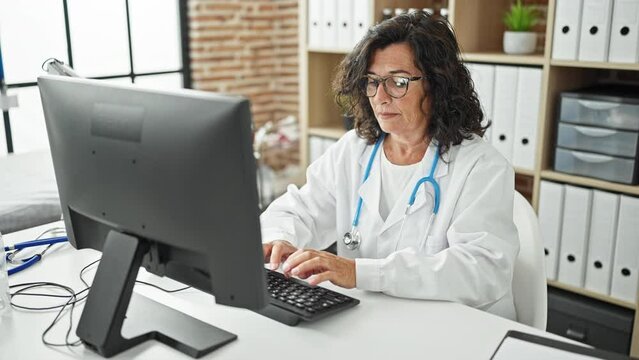 Middle age hispanic woman doctor using computer working smiling at the clinic
