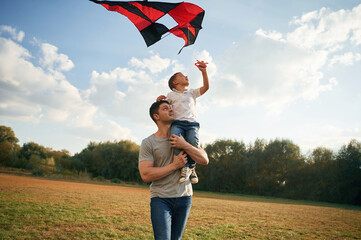 Red colored kite in hands. Father and little son are playing and having fun outdoors