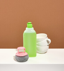 Green detergent, steel abrasive dishwashing sponge, clean white cups on the table.