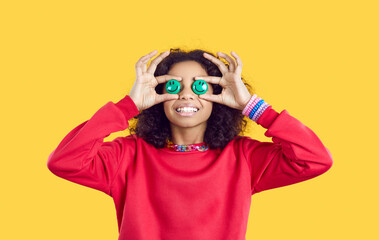 Happy child with funny green emoji eyes. Joyful African American kid with emoticon eyes smiling and sharing good mood with you. Cute little girl in red sweatshirt holding two smiley faces on her eyes