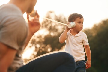 Fun, holding and using string can phone. Father and little son are playing outdoors