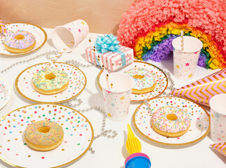 Colorful bright birthday party composition. Delicious, sweet, fresh donuts with colored sprinkles on festive plates, beautifully wrapped gifts, bright colorful rainbow pinata.