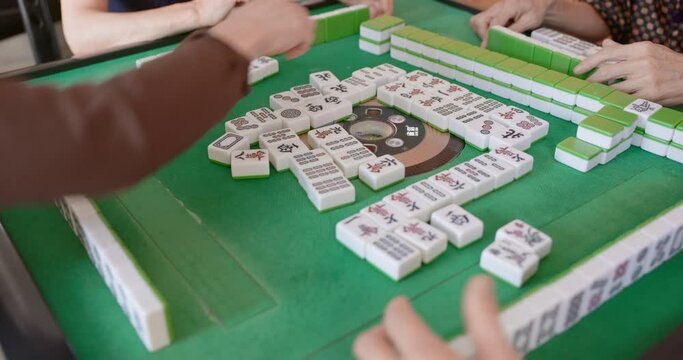 Selective focus with closeup of mahjong tiles and the player's hand tapping on gambling table.