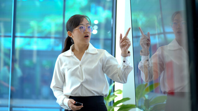 young asian business woman standing in front of television screen giving presentation and Explaining Graphs in office . speaker with whiteboard presenting  idea to colleagues in meeting - Powered by Adobe