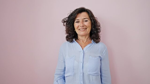 Middle age hispanic woman taking glasses of standing over isolated pink background