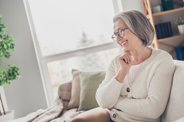 Obraz premium Photo of pretty adorable senior lady dressed white cardigan sitting sofa watching movie indoors house room