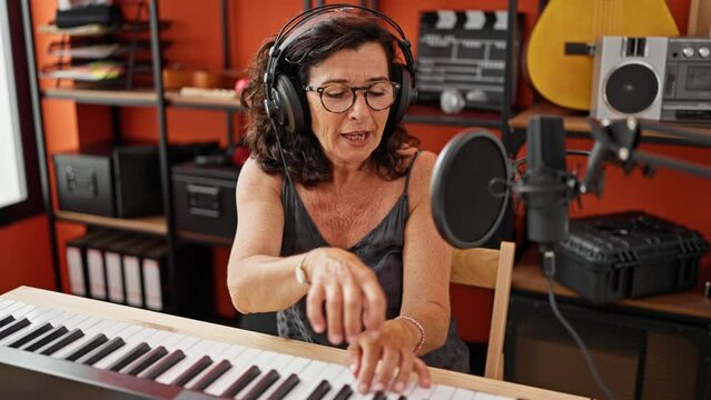 Middle age hispanic woman musician singing song playing piano at music studio