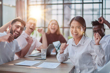 group of different business people celebrating victory while sitting at table in modern office