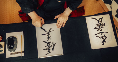 High Angle Footage of a Japanese Artist Working on a Commissioned Calligraphy Work for a Client. Adult Calligrapher Sitting in a Traditional Studio, Writing Kanji Symbols with Ink on a Piece of Paper