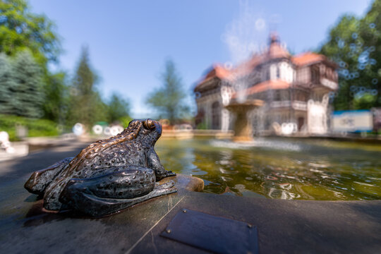 Swieradow Zdroj, Poland; Sculpture of a frog by the fountain - the spa house "Szarotka" in Swieradow Zdroj in the background - very shallow depth of field