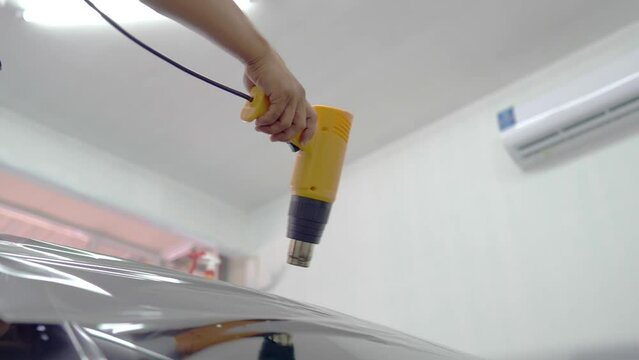 Automotive technicians use a hot air blower on car windows to prepare for installing car window film.