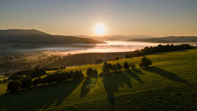 Sunrise in czech mountains with foggy valley with village and meadows. 