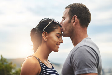 Forehead, love or couple kiss in nature for date, wellness or care on summer romance or adventure. Peace, smile or man with happy woman on outdoor holiday vacation together to bond, support or relax