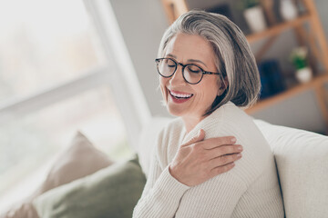 Photo of sweet adorable senior lady dressed white cardigan eyewear embracing herself closed eyes indoors house room - obrazy, fototapety, plakaty