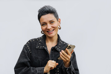 Portrait of cheerful  girl a short gray hair using smartphone. Woman in fashion jean jacket on a white background. Trend women's haircut hairstyle. - obrazy, fototapety, plakaty