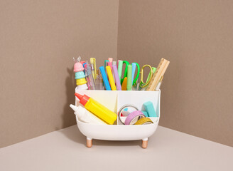 Various stationery lie in a tub shaped stand. Scissors, pencils, pens, colored tape, glue and a...