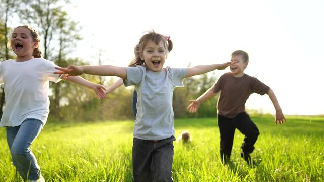 group of children running in the park. happy family baby kid dream concept. kindergarten. children hands to the sides play pilots plane run sun on the grass in the summer in the park