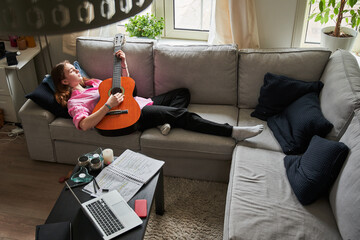 Relaxed happy female musician playing guitar with pleasure while laying