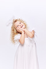 Beautiful, smiling, cute little girl child in white dress in image of angel standing isolated over white studio background. Concept of childhood, imagination, fantasy, fashion and beauty, holidays
