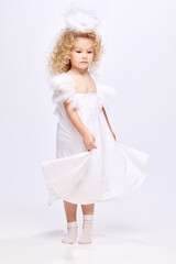 Beautiful, cute little girl child in white dress in image of angel standing isolated over white studio background. Concept of childhood, imagination, fantasy, fashion and beauty, holidays