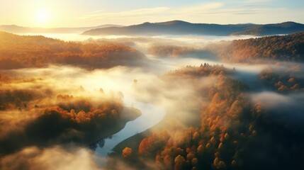 Obraz premium An aerial view of the forest with the sun behind the mist all around, colored autumnal trees in the morning light.