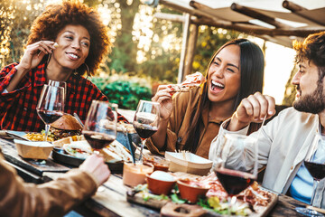 Multiracial friends having fun at barbecue dinner party in garden restaurant - Millennial people cheering red wine sitting at outside bar table - Youth lifestyle, food and beverage concept - obrazy, fototapety, plakaty