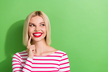 Portrait of gorgeous nice woman with bob hairstyle wear striped shirt look empty space finger cheek isolated on green color background