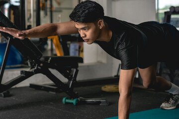 A young handsome asian man executes a prone two point bridge exercise on the mat at the gym. Advanced and difficult core exercises.