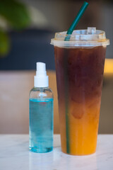 Instant antiseptic hand sanitizer mist spray put with iced black coffee mix with orange juice. Close up