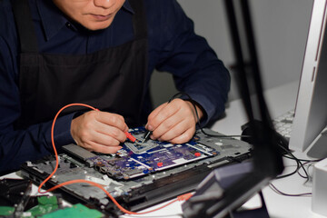 A young man who is a computer technician A laptop motherboard repairman is using an IC meter to find defects on the motherboard to repair on his table. Repair boards with technology