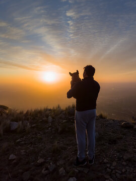 Silhouette of a man with his dog, in a majestic sunset over the mountain. Vertical photo.