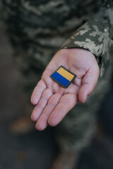 A Ukrainian military man holds the emblem of the national flag in his hand as a symbol of strength. War in Ukraine. Dramatic background, warm colors