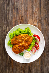 Crispy breaded seared chicken cutlet with lettuce and tomatoes on wooden table
