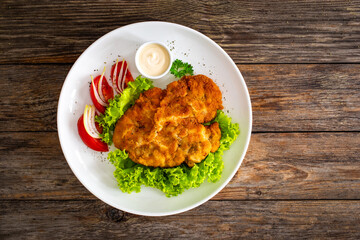 Crispy breaded seared chicken cutlet with lettuce and tomatoes on wooden table
